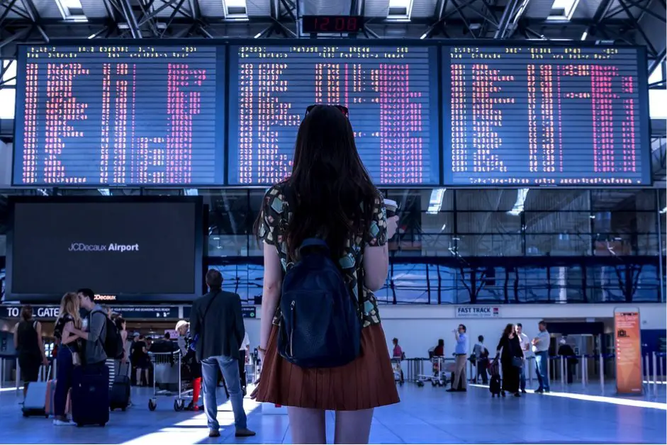 Girl standing in front of airport flight arrivals-departures board.